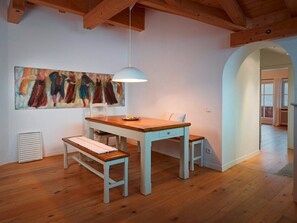 Et spiseområde med et træbord og bænk, en hængende lampe og et farverigt abstrakt billede på væggen.