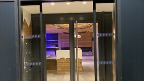 Entrada de un hotel de diseño moderno, con puerta de vidrio y marco metálico, mostrador de recepción en el interior y techo con una lámpara de techo original.