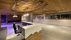 Un vestíbulo amplio con diseño moderno, que incluye una recepción, zona de estar y una estructura de techo geométrica.
