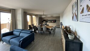 Una sala de estar moderna con un sofá azul, un comedor con mesa y sillas de madera, y una cocina al fondo.