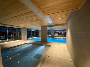 Ein moderner Innenpool mit Holzboden und Glaswänden, der einen Blick ins Freie bietet.