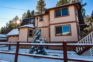 A two-story building with a wooden exterior, a covered porch, and a snow-covered lawn. - Bufflehead Cottage by Destination Big Bear: Pool Table! Spa! Mountain Views! (Big Bear City)