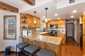 A modern kitchen with granite countertops, wooden cabinets, and stainless steel appliances. - Bufflehead Cottage by Destination Big Bear: Pool Table! Spa! Mountain Views! (Big Bear City)