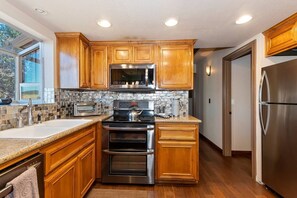 A modern kitchen with wooden cabinets, stainless steel appliances, and a stone backsplash. - Bufflehead Cottage by Destination Big Bear: Pool Table! Spa! Mountain Views! (Big Bear City)