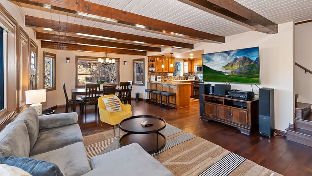 Een ruime woonkamer met een grote eettafel, comfortabele zitplaatsen, een keuken met houten kastjes en een tv waarop een mooi landschap te zien is.