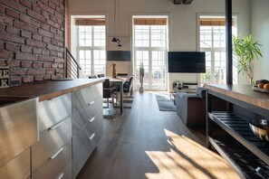 Une cuisine moderne avec un mur en briques, de grandes fenêtres et un téléviseur à écran plat.