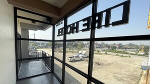 Ett hotellrum med stora fönster som ger utsikt över en parkeringsplats och de omgivande byggnaderna.