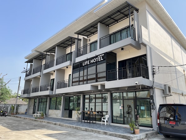 A multi-story building with a sign reading "LIFE HOTEL". It features balconies, large windows, and outdoor seating.