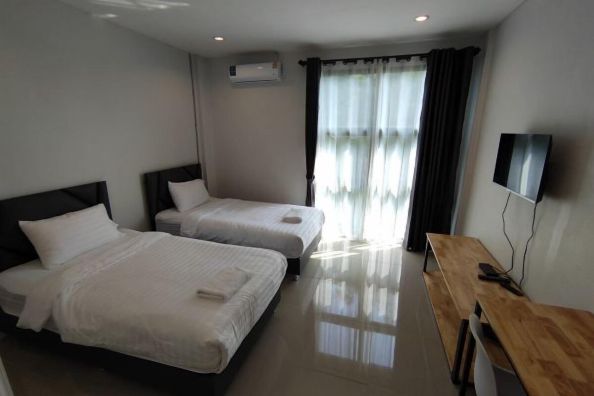 Habitación de hotel con dos camas, un escritorio, un televisor y una ventana con cortinas.