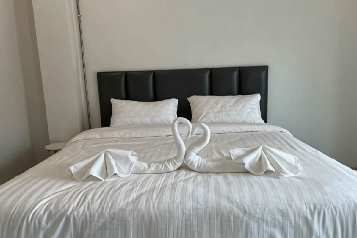 Una cama con cabecera negra, almohadas blancas y una decoración de toalla con forma de cisne.