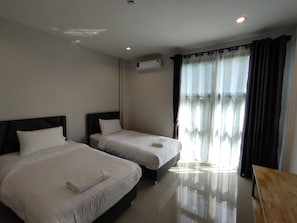 A hotel room with two beds, a wooden table, and a window with curtains.
