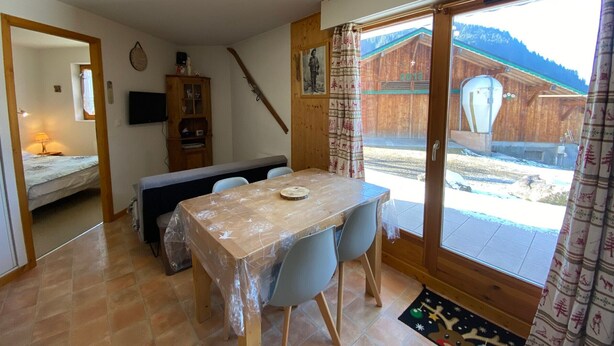 Une pièce chaleureuse avec une table à manger en bois, des chaises, un banc et une porte-fenêtre coulissante donnant sur un espace extérieur enneigé.