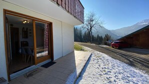 Un bâtiment doté d’une entrée avec une porte en verre, d’un patio carrelé et offrant une vue sur un paysage enneigé avec des montagnes en arrière-plan.
