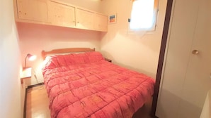 Un dormitorio pequeño con una cama individual, una mesita de noche, una lámpara, una ventana y una puerta.