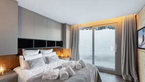 A modern hotel room with a large bed, a bedside table with a lamp, a wardrobe, and a view of a snowy landscape through a glass door. - Prestigious chalet with jacuzzi - 10 guests (Courchevel 1550)