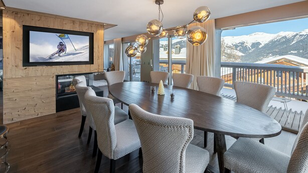 A modern dining area with a large wooden table, upholstered chairs, and a television mounted on the wall. - Prestigious chalet with jacuzzi - 10 guests (Courchevel 1550)