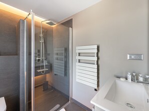 Ein modernes Badezimmer mit einer Glaskabine zur Dusche, einem weißen Waschbecken und einem Handtuchhalter.