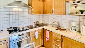 Een keuken met houten kastjes, een roestvrijstalen afzuigkap, een spoelbak, een broodrooster en een koffiezetapparaat.