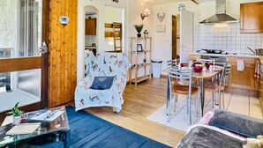 Een gezellige woonkamer met een gestreept fauteuil, een eethoek met een ronde tafel, en een keuken met moderne apparatuur.