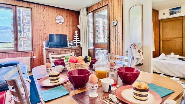 Een gezellig eetgedeelte met houten wanden, een televisietoestel en uitzicht op een bergachtig landschap.