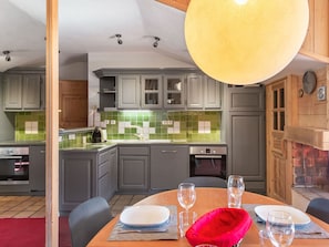 A modern kitchen with grey cabinets, a green tiled backsplash, and a dining area with a wooden table set for two. - Cozy apartment in Courchevel 1850 with sauna and parking (Courchevel 1850)