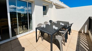 A patio with a table and chairs, a sliding glass door, and a small window. - Saint Cyprien - 2-Bedroom Apartment for 6 - Shared Pool, Terrace, Parking (Saint-Cyprien)