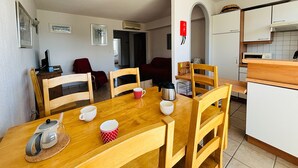 A dining area with a wooden table, chairs, and a kettle. There is a kitchen area with cabinets and a microwave. - Saint Cyprien - 2-Bedroom Apartment for 6 - Shared Pool, Terrace, Parking (Saint-Cyprien)