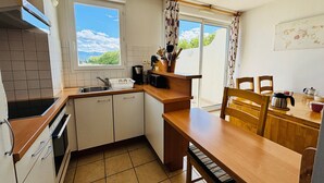 A compact kitchen with a window, a sink, a stove, and a dining area with chairs and a table. - Saint Cyprien - 2-Bedroom Apartment for 6 - Shared Pool, Terrace, Parking (Saint-Cyprien)