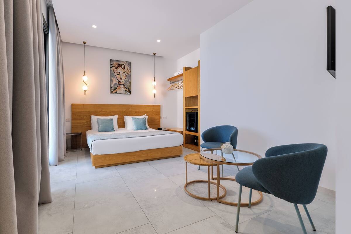 Ein modernes Hotelzimmer mit einem großen Bett, einem kleinen Tisch, zwei Stühlen und einem an der Wand befestigten Regal.
