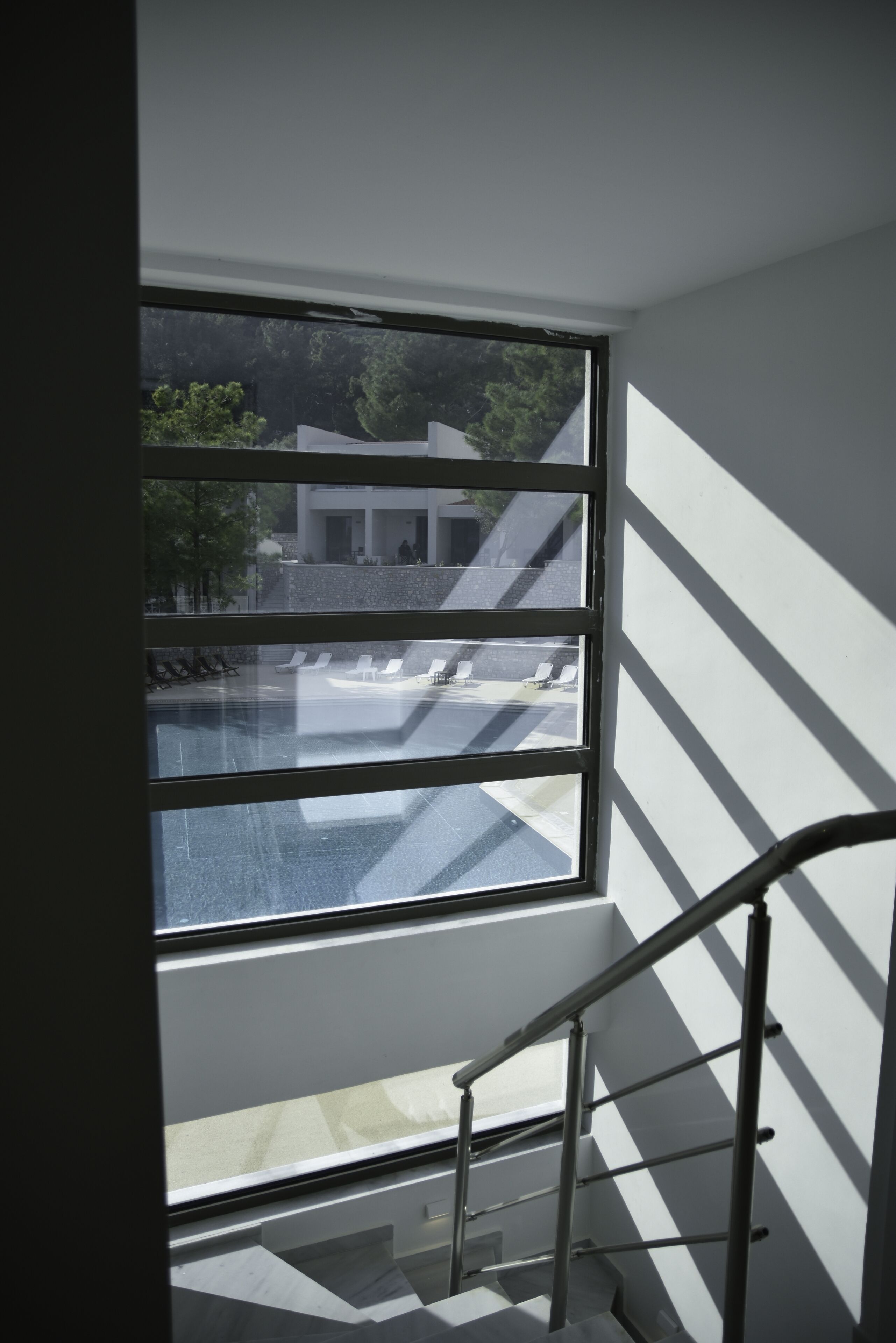 Un interior moderno con un amplio ventanal, una escalera de metal y vistas a un edificio y árboles.