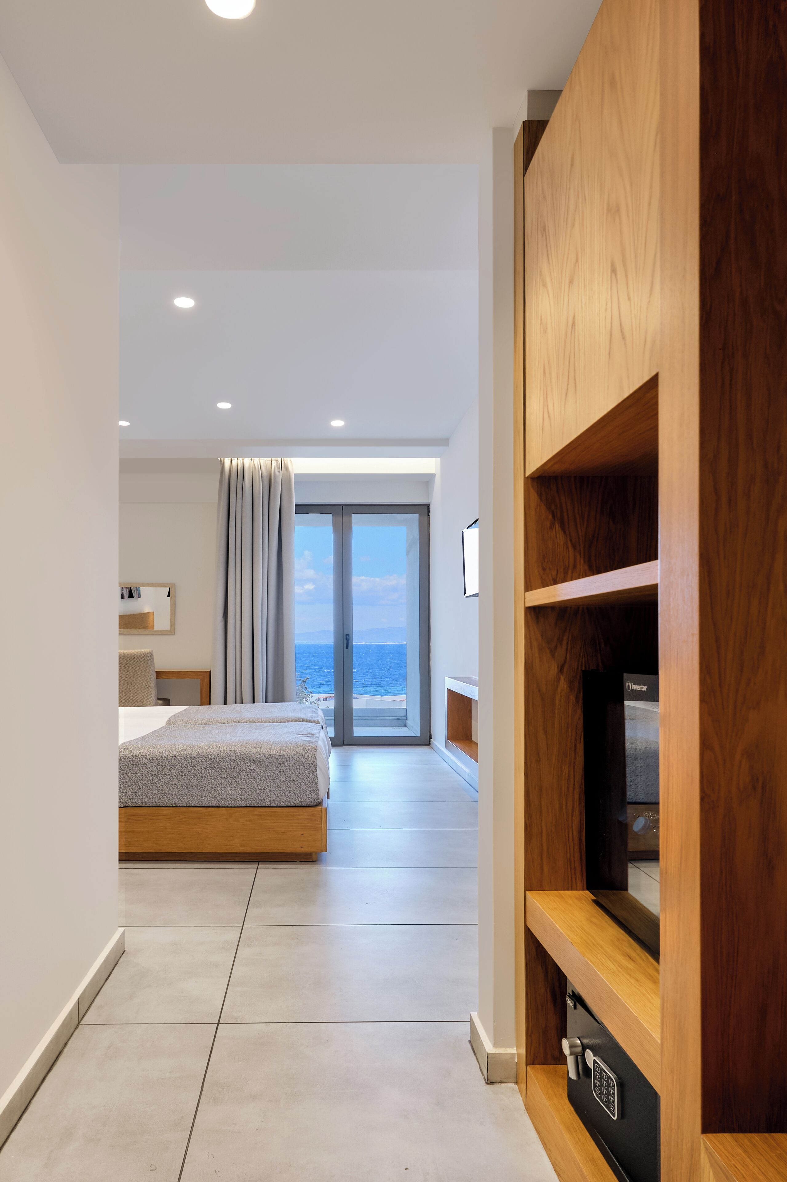 A modern hotel room with a bed, a TV, and a view of the sea.