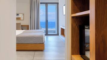 A modern hotel room with a bed, a TV, and a view of the sea.