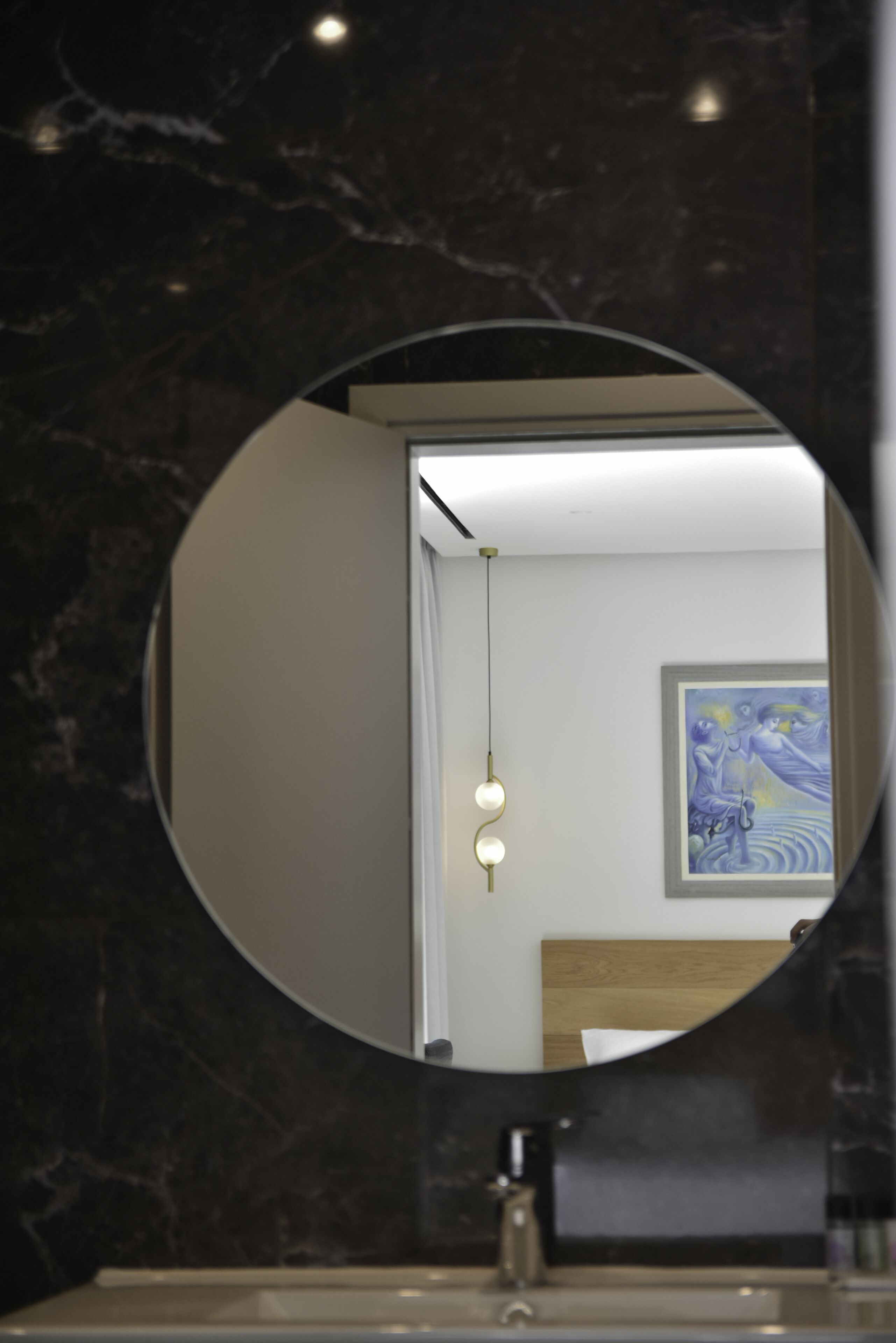 Un baño con pared de mármol, espejo redondo, lavabo y un cuadro en la pared.