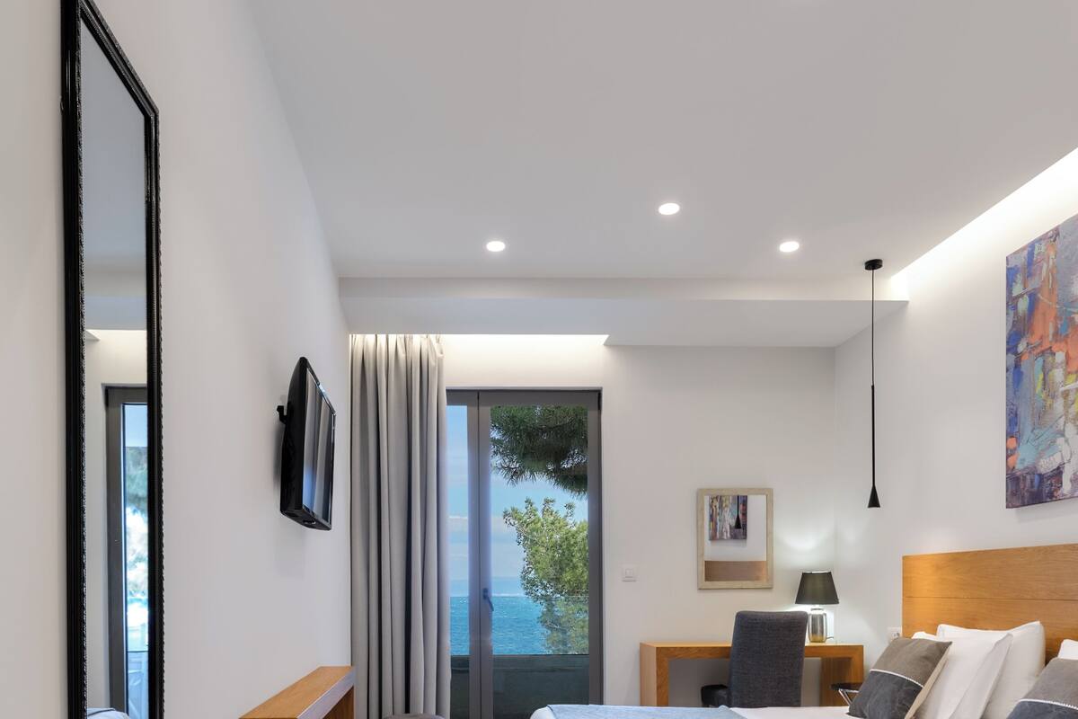Ein modernes Hotelzimmer mit einem großen Bett, einem Schreibtisch, einem Sessel, einem Fernseher und Meerblick.