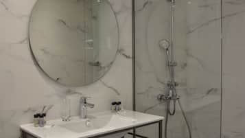 Un baño moderno con tocador de mármol, un espejo redondo, cabina de ducha con paredes de vidrio y toallas ordenadas en un perchero.