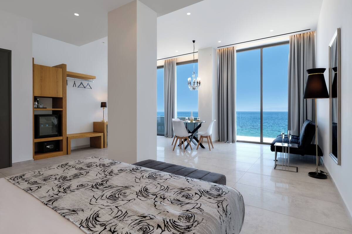 Ein modernes Hotelzimmer mit einem großen Bett, einem Essbereich mit Meerblick und einem Balkon mit Tisch und Stühlen.