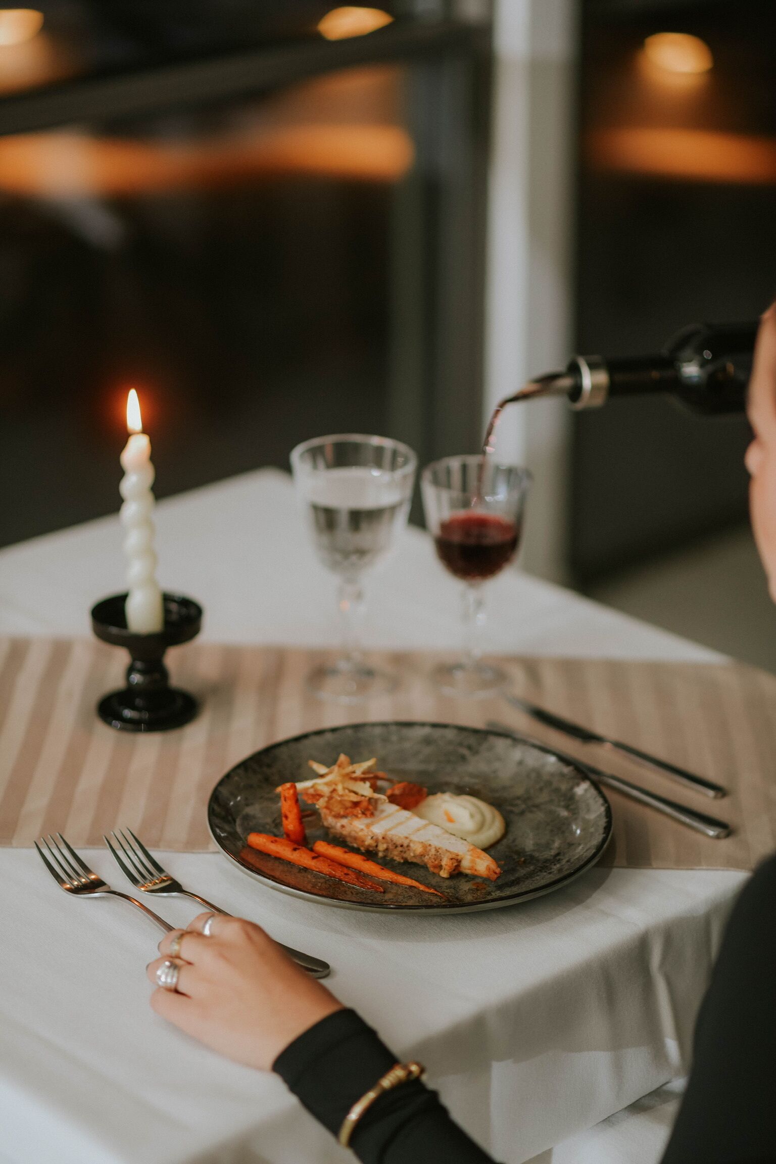 A dining table with a candle, two glasses, and a plate of food.