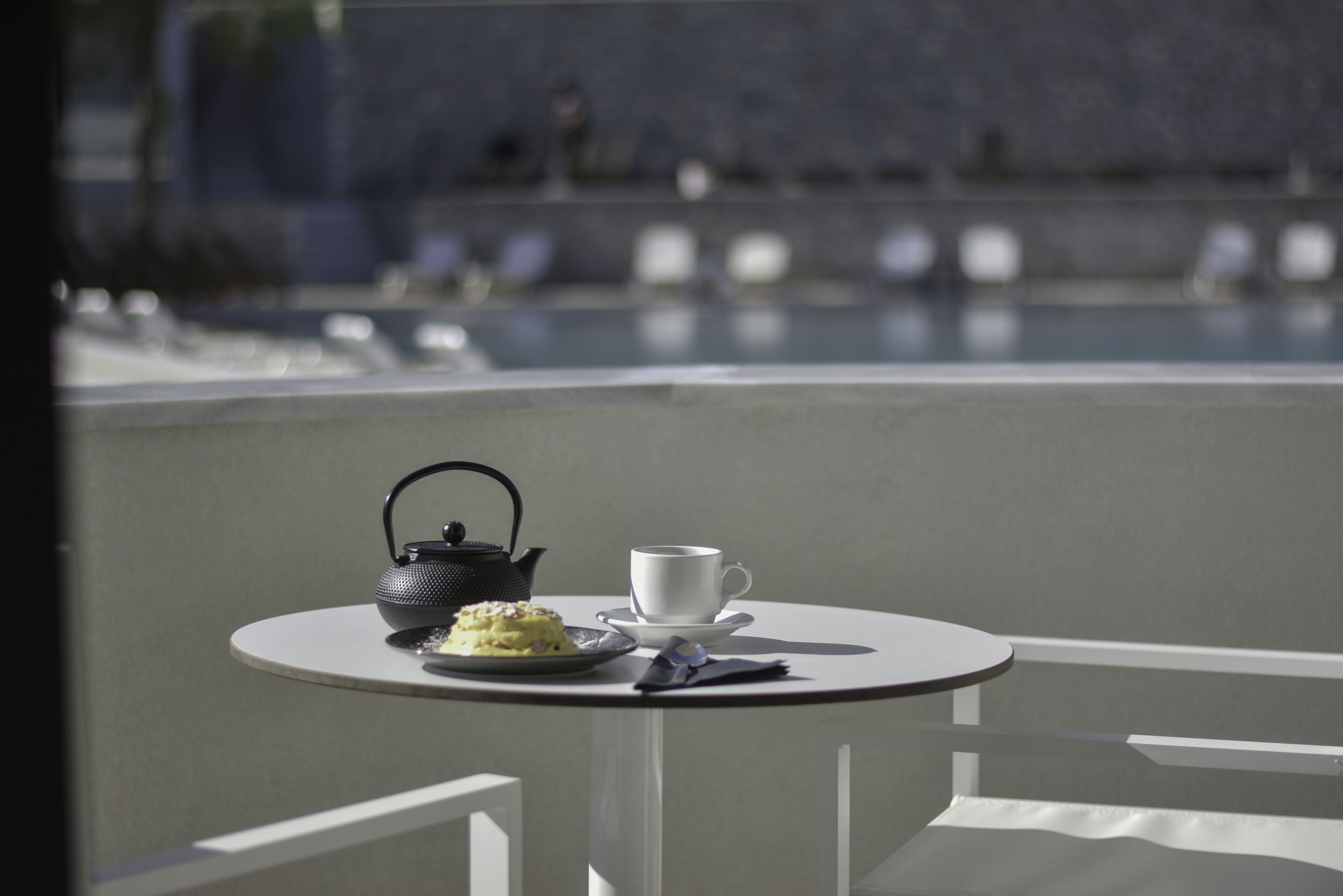Une table ronde avec une tasse blanche, une théière noire et une assiette de nourriture.