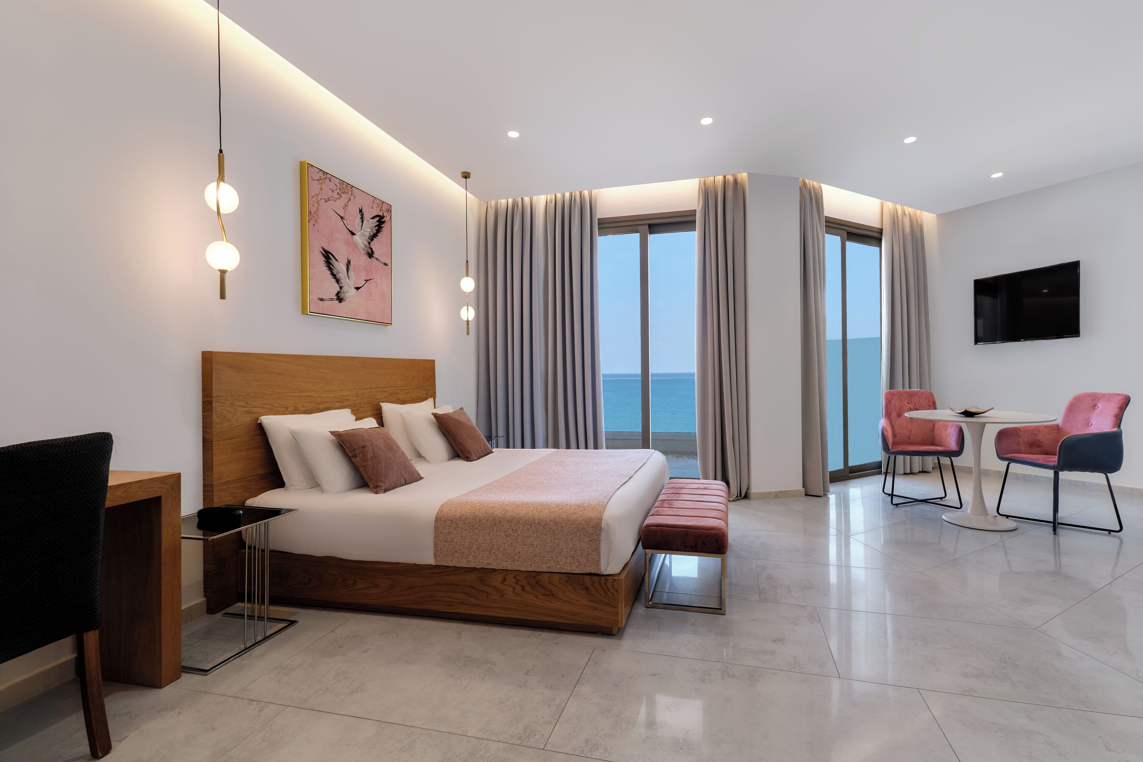 Ein modernes Hotelzimmer mit einem großen Bett, einem Schreibtisch, einem Sessel, einem kleinen Tisch und einem Fernseher.