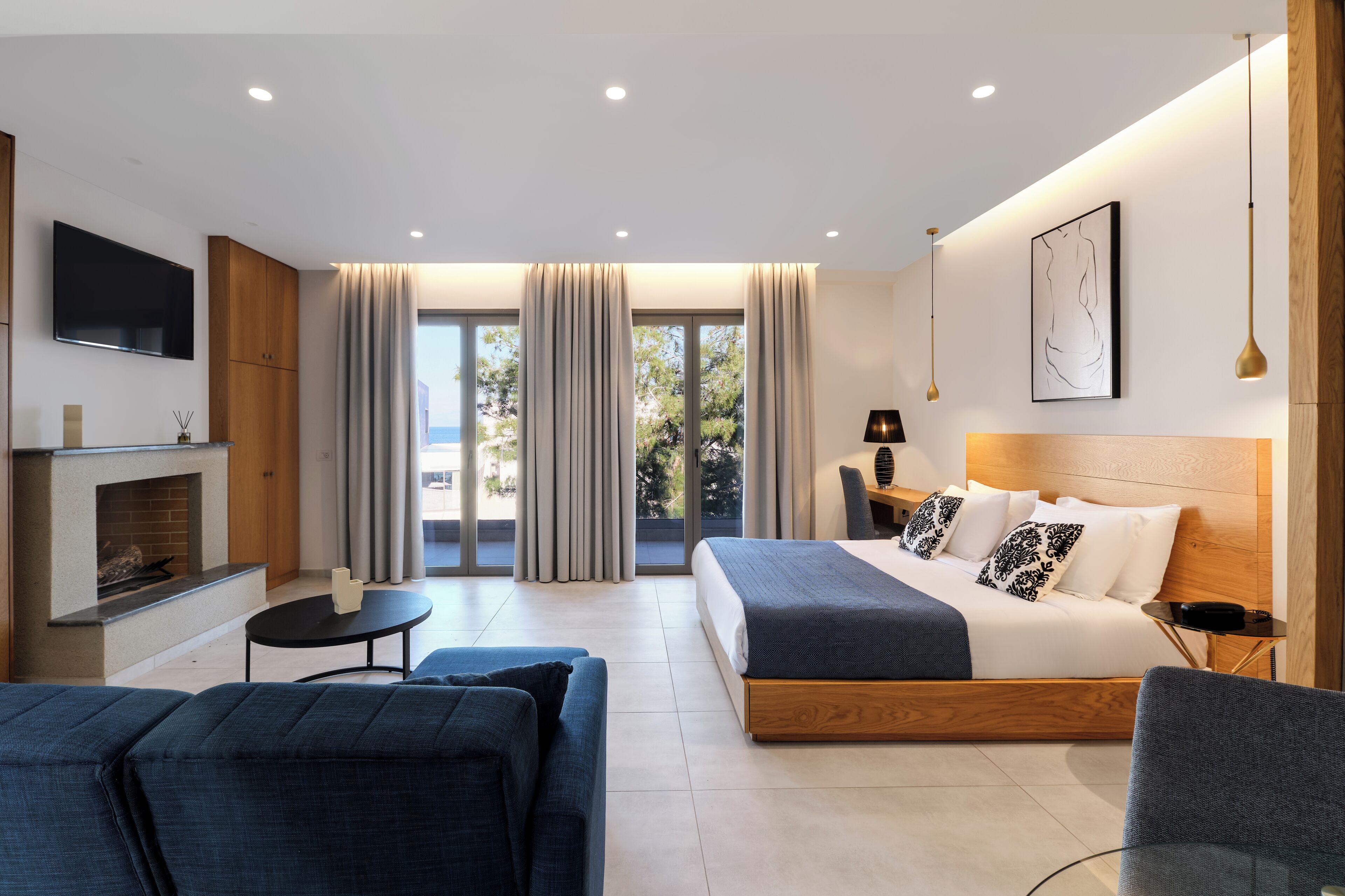 A modern hotel room with a bed, a TV, a fireplace, and a balcony with curtains.