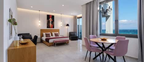 A modern hotel room with a bed, bedside table, and a dining area with chairs and a table.