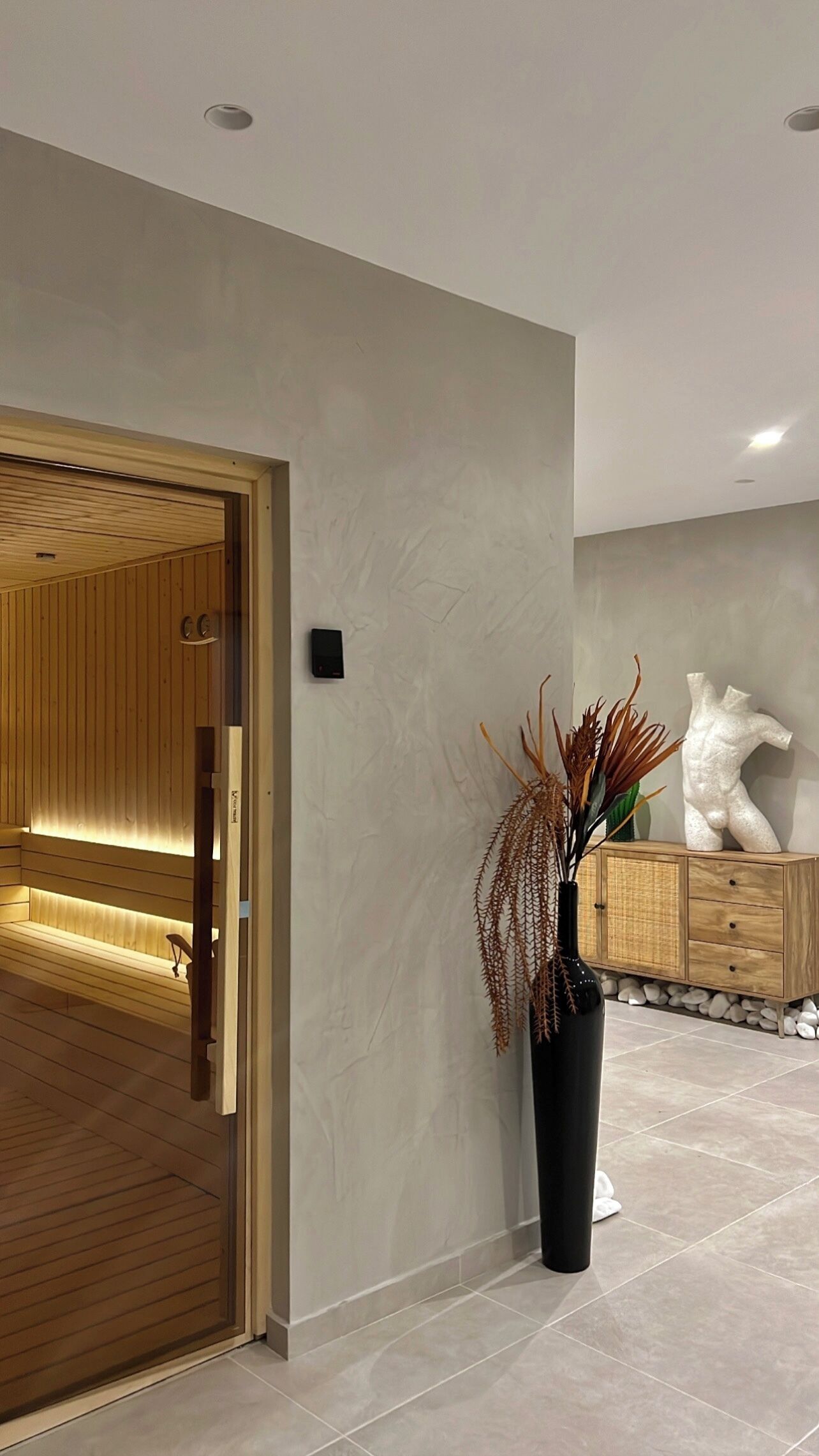 A modern interior with a wooden bench, a black vase with dried plants, and a white abstract sculpture on a wooden cabinet.