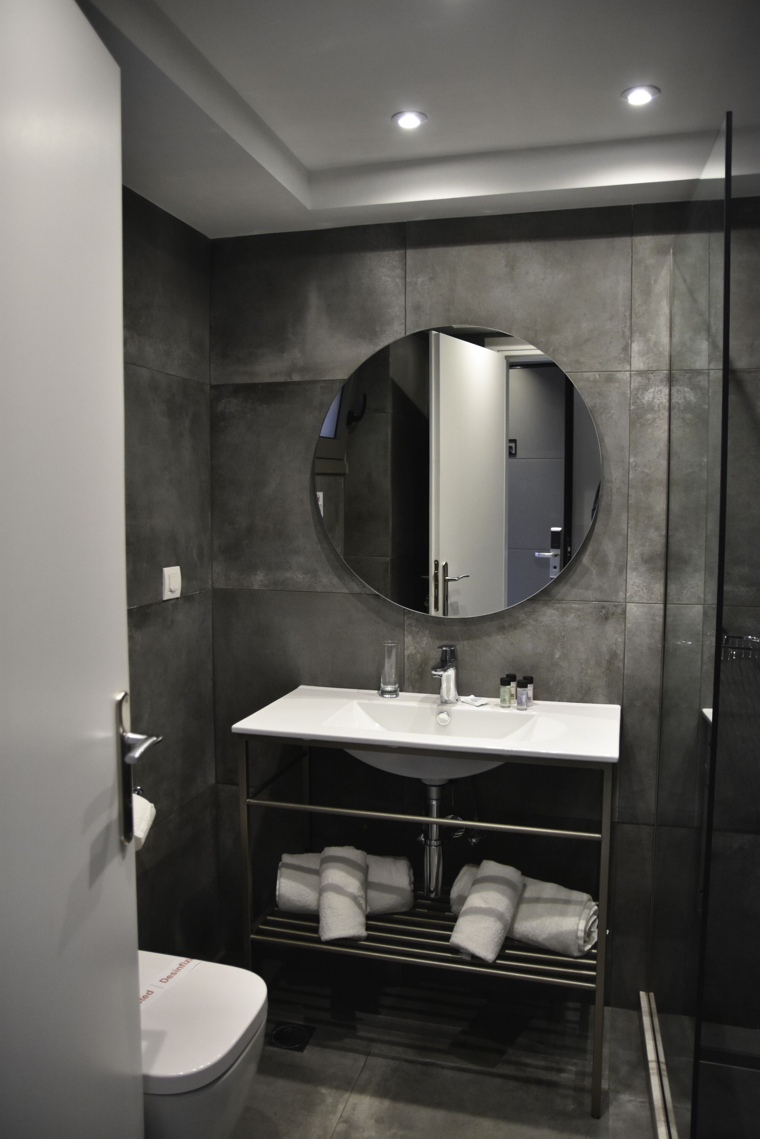 A modern bathroom with a white sink, a round mirror, and a towel rack.
