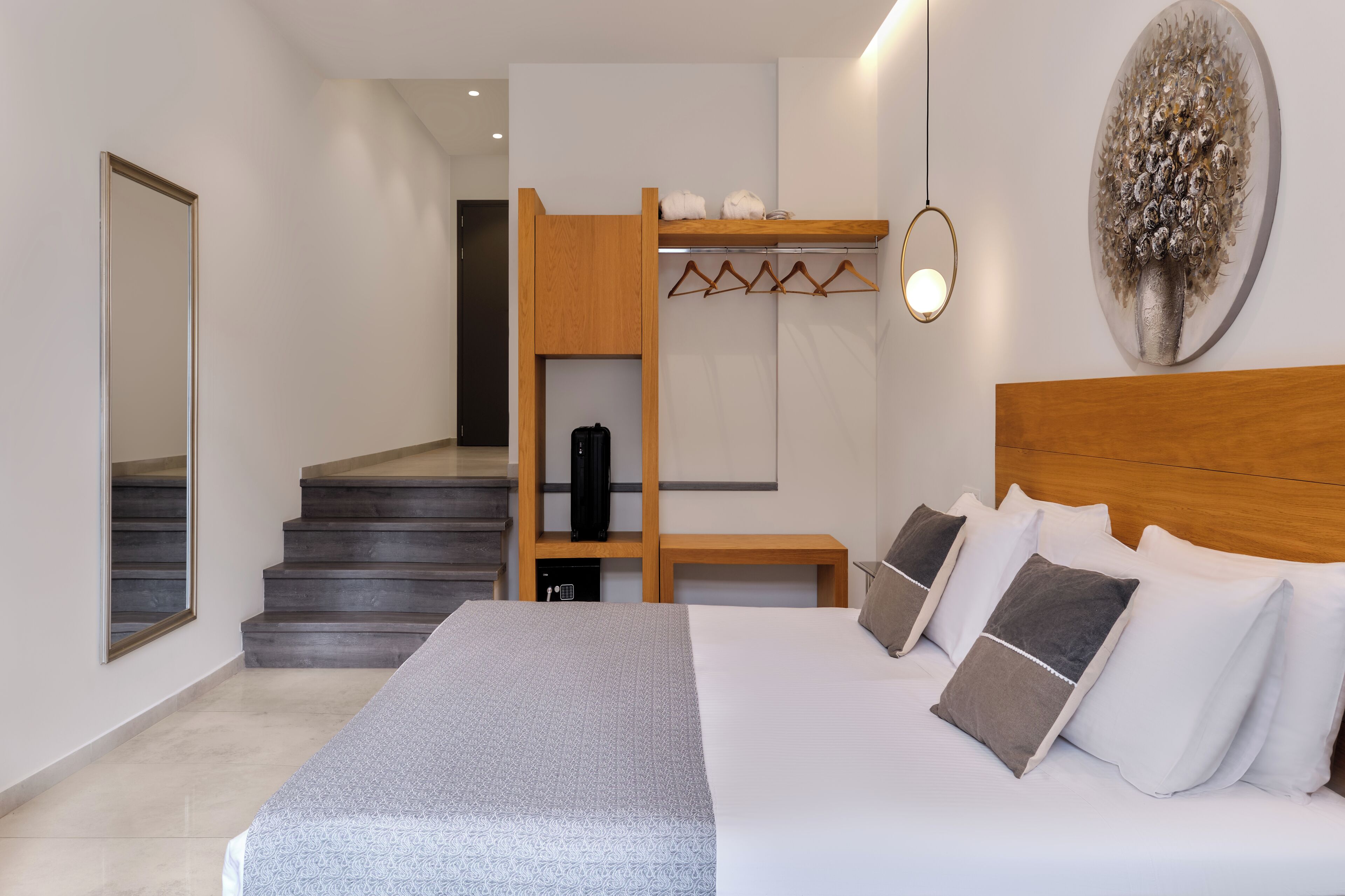Une chambre d’hôtel moderne dotée d’un grand lit, d’une tête de lit en bois, d’un porte-manteau et d’un escalier menant à un étage supérieur.