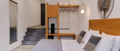 A modern hotel room with a large bed, a wooden headboard, a coat rack, and a staircase leading to an upper level.