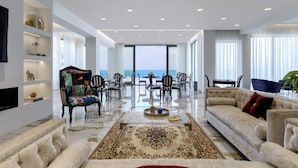 A spacious living room with a large window, a sofa, a coffee table, and a dining area with chairs and a table. - Mythical Coast Wellness Retreat (Lesvos)