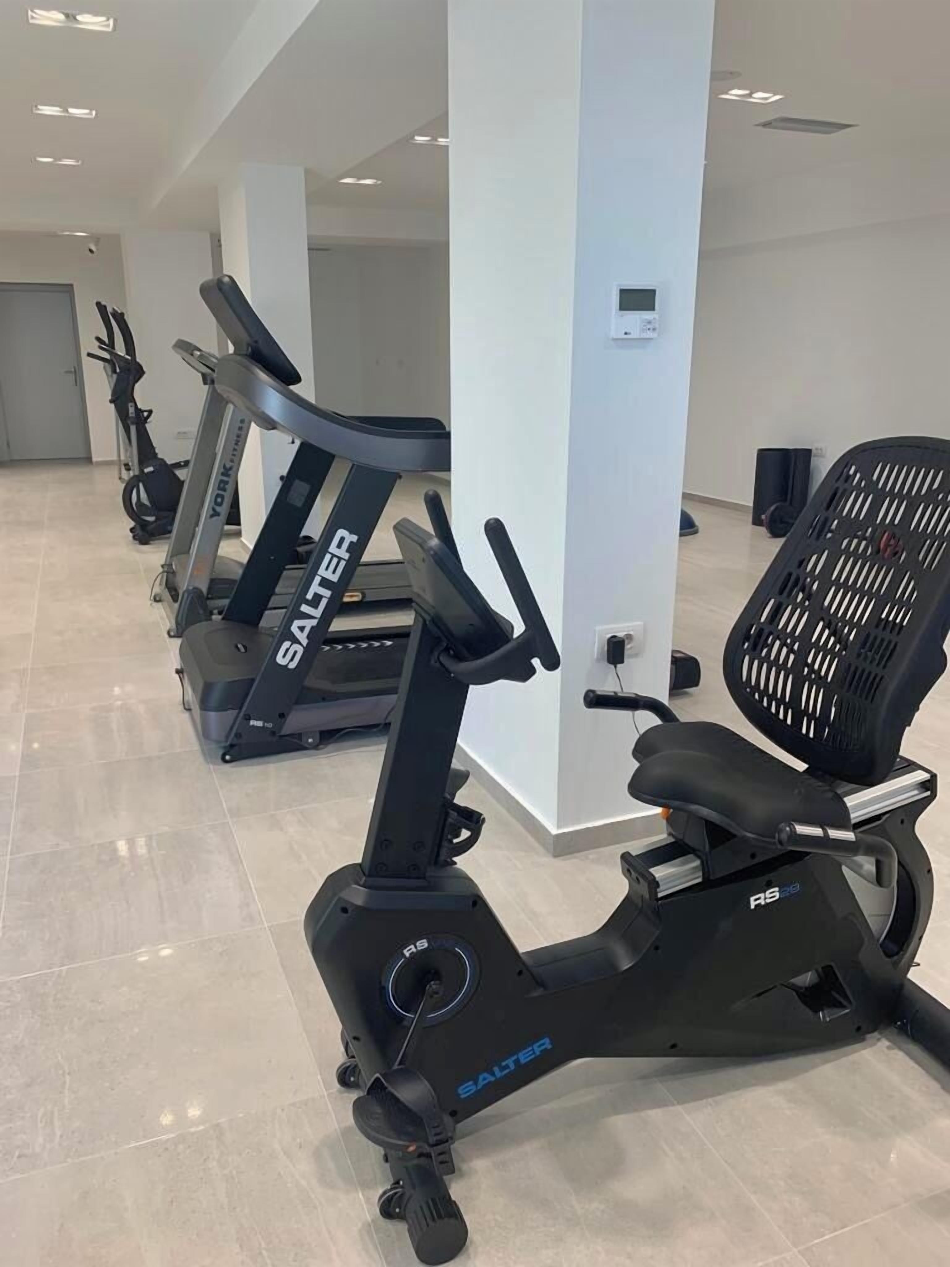 Varias bicicletas estáticas en un gimnasio con suelo de baldosas y paredes blancas.