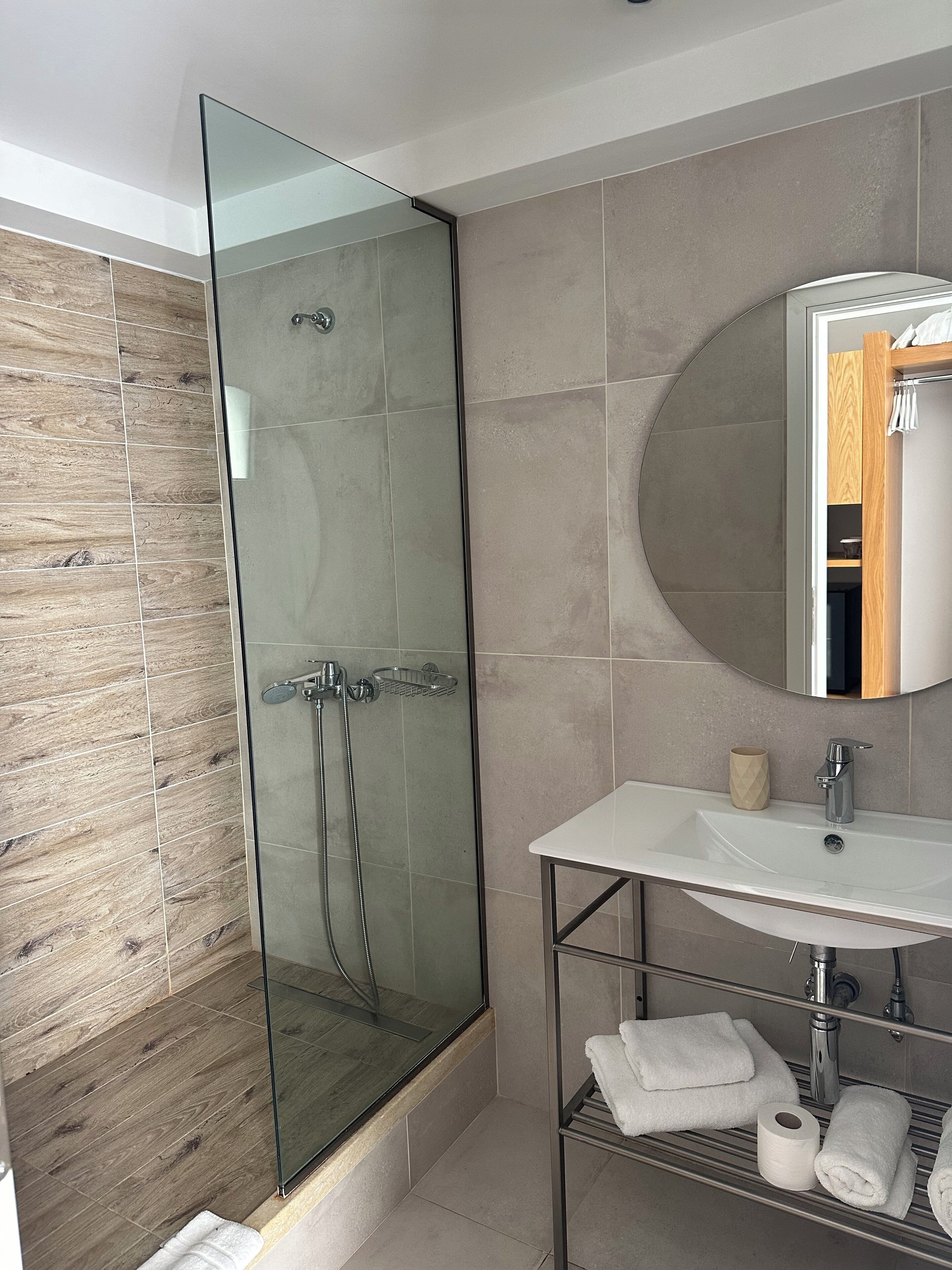 Un baño moderno con ducha envuelta en vidrio, un lavamanos blanco y un mueble de tocador de madera.