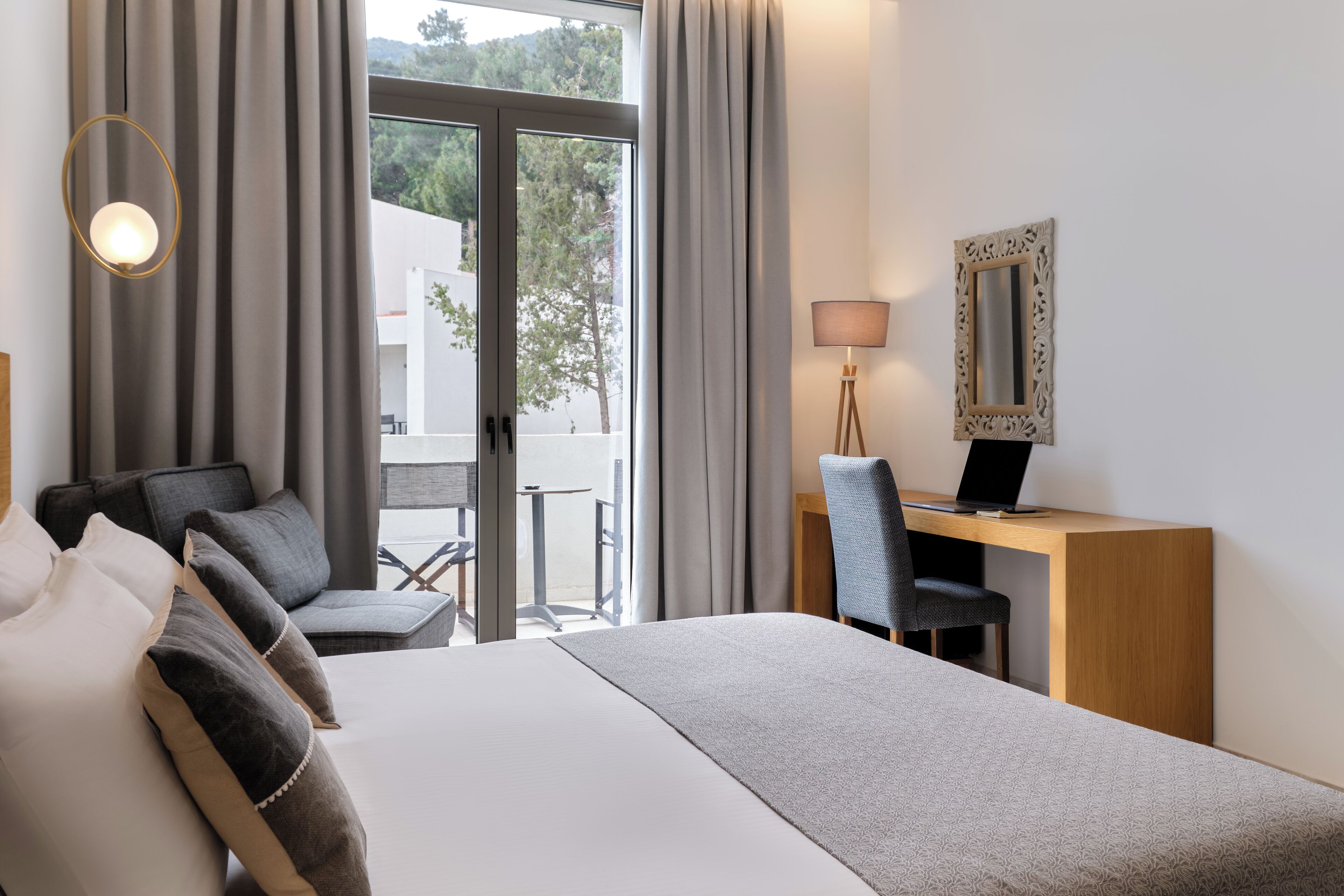 Ett hotellrum med en säng, ett skrivbord, en stol, en lampa och en spegel.