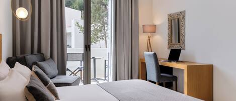 A hotel room with a bed, a desk, a chair, a lamp, and a mirror.